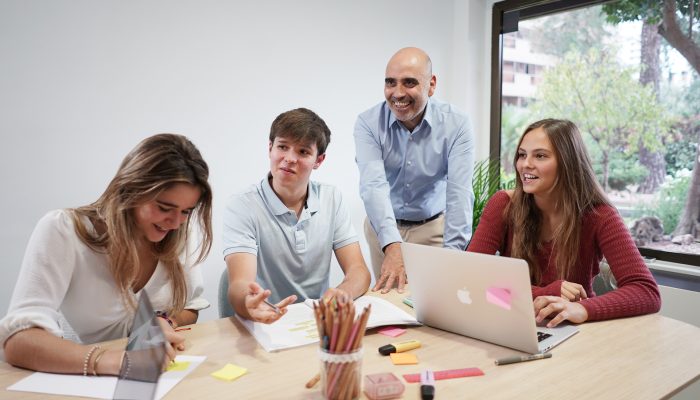 profesor en una mesa de trabajo del aula con 3 chicos